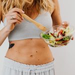 Young woman in sports attire holding a fresh salad bowl, promoting a healthy lifestyle.