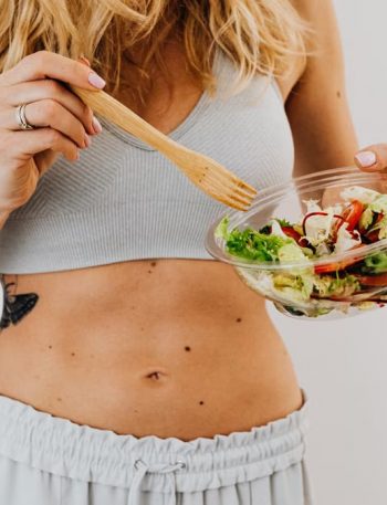 Young woman in sports attire holding a fresh salad bowl, promoting a healthy lifestyle.