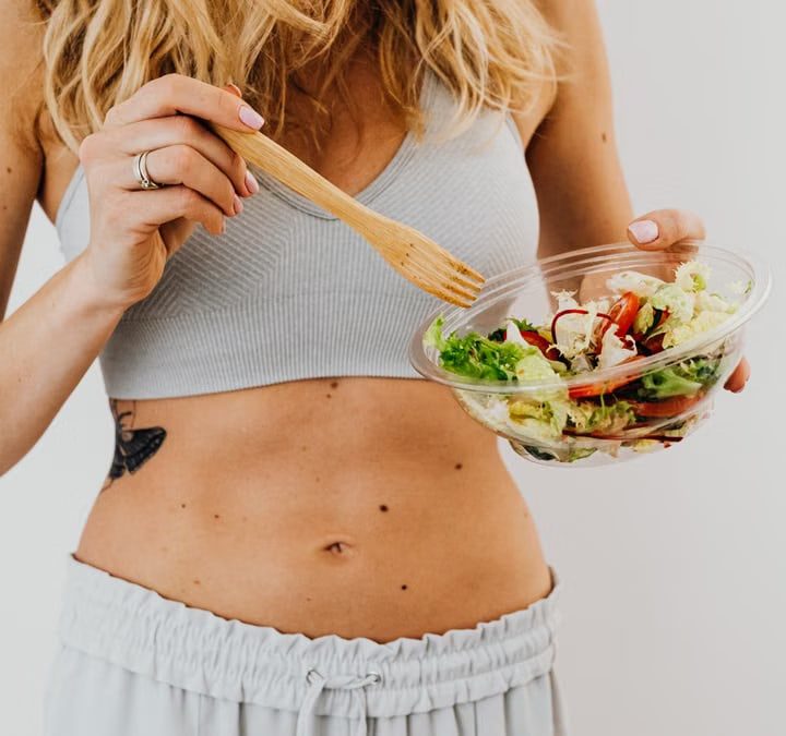 Young woman in sports attire holding a fresh salad bowl, promoting a healthy lifestyle.