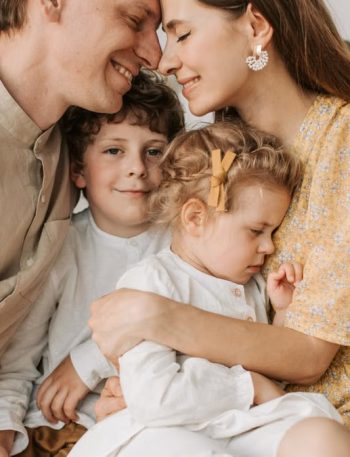 A loving family of four shares a tender moment in a cozy indoor setting, embracing and smiling.