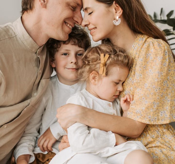 A loving family of four shares a tender moment in a cozy indoor setting, embracing and smiling.